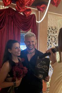 Alexa and Nick standing with flowers on Valentine’s Day while recording a video message to preserve their feelings for the future.