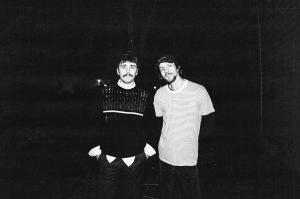 Zach Benson and Tyler Adlam pose as SAID, NEVER in black-and-white against a black background. Zach wears a black sweater over a white button-down shirt, while Tyler wears a striped tee over a black long-sleeve shirt.