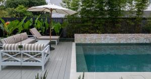 Fully tiled compact plunge pool in Sydney backyard featuring natural stone wall, timber decking and private tropical landscaping.