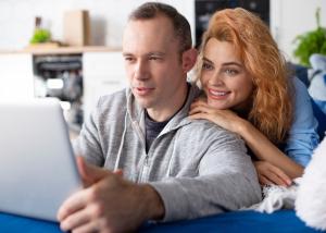 A couple sitting together on a couch, engaging in a video call on a laptop with an older woman waving on the screen, illustrating telehealth connectivity and family support.