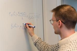 Man writes a physics equation on a white board.