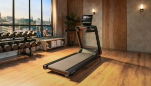 An empty treadmill in a small gym, with dumbbells and towels nearby.