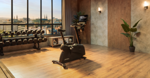 An empty upright bike in a small gym, with dumbbells and towels nearby.