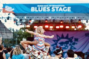 Young child in an America outfit sitting on shoulders of an adult dancing to music at Waterfront Blues Festival