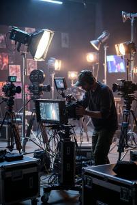 Videographer adjusting professional camera with monitors and lights in a dimly lit studio, illustrating AI's role in disrupting and enhancing creative workflows in 2026.