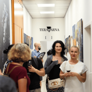 Exhibition visitors stand in a bright gallery hallway with artworks on both walls and the TERAVARNA logo visible at the far end.