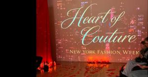 A clear view of the Heart of Couture New York Fashion Week logo and branding on a digital screen behind a candle-lit runway.