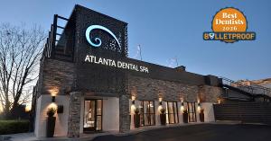 Exterior view of the Atlanta Dental Spa building in Poncey-Highland at dusk, featuring a prominent "Best Dentists 2026 - Bulletproof" award badge in the top right corner, alongside its illuminated sign and modern stone and metal architecture.