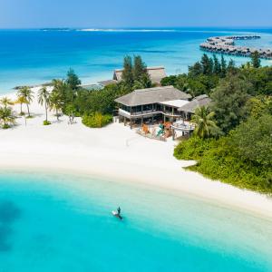 A paddleboarder in a blue lagoon to the island backdrop of a white beach and tropical fauna at Grand Park Kodhipparu, Maldives