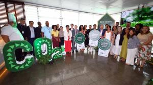 A group of representatives from SESC, SENAC, and GI International standing together in a bright hall, holding circular green and white Carbon Neutral certification signs. Large green decorative letters spelling "CO2" with a downward arrow are positioned in foreground.