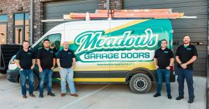 The Meadows Garage Doors team standing together in front of a branded company truck featuring the Meadows Garage Doors logo and green wrap design.