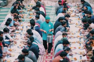 Volunteers distributing Iftar meals to fasting men seated in rows during a Ramadan charity event.