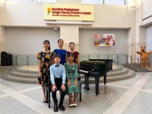 Five young EAMA piano students posed beside a grand piano in the lobby of NewYork-Presbyterian Morgan Stanley Children's Hospital at Columbia University Medical Center.