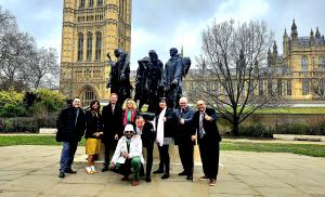 Nine professionals posing with thumbs up in front of the Burghers of Calais statue in Victoria Tower Gardens, Westminster, London, Feb 2026.