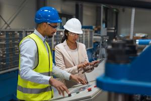 Factory technicians wearing safety helmets and protective equipment reviewing automation controls and digital data on a tablet inside a modern industrial facility, illustrating the importance of human expertise and technical support in automated manufactu