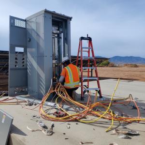 Electrician facing a solar combiner box while securing and wiring bundled electrical conductors at a commercial solar project.