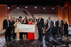 Group of gala organizers, donors and physicians stand on stage under warm lights holding a large ceremonial cheque for $1,813,325 for Surrey Hospitals Foundation’s Celebration of Care Gala, with confetti on the floor and “Journey” branding in the backgrou