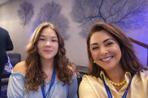 Carissa Düring (on the left) and Suely Castro (on the right) smiling together at an event, both wearing conference badges.