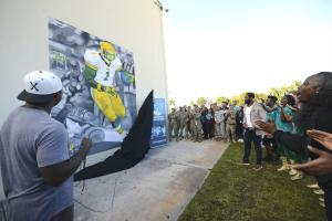 Artist Ju Reams (left) unveils the mural he created at the high school where former NFL safety Nick Ferguson (center) went to school and got his start in football.