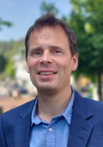 The photo shows Enerin CEO Arne Høeg, who is also a mechanical and process engineer, and inventor. The photo shows his head and shoulders. He is wearing a medium-coloured blue jacket with a lighter blue shirt, and is shown smiling and relaxed. In the back