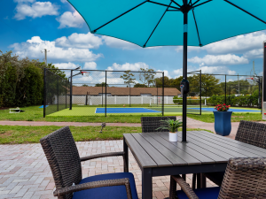 outdoor table with chairs and umbrella with a tennis and basketball court in the background