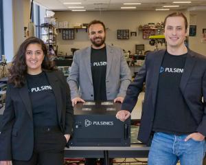 Three smiling businesspeople pose near their industrial machine