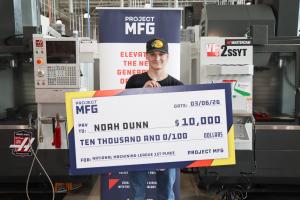 A student standing in a machining lab holding a large check made out to him for $10,000