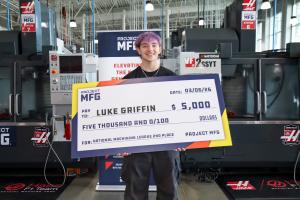 A student standing in a machining lab holding a large check made out to him for $5,000 and says National Machining League 2nd Place