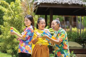 Group of individuals in colorful Songkran outfits holding water guns and enjoying a water activity in a tropical outdoor garden setting.