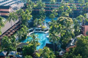 Aerial view of a tropical resort with multiple swimming pools surrounded by tall palm trees, greenery, and multi‑story buildings.