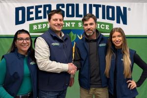 Co-owners Taylor and Mary Goodrich, right, shake hands with Kris Goodrich, left, with wife and co-founder Jaime Goodrich, in front of the Deer Solution logo backdrop.