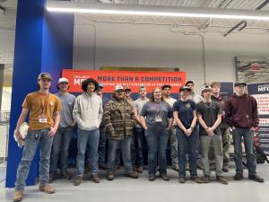 A group of high school students stand together in front of a Project MFG banner at the Advanced Technical Skills Institute at Metropolitan Community College–Penn Valley during a student welding competition.