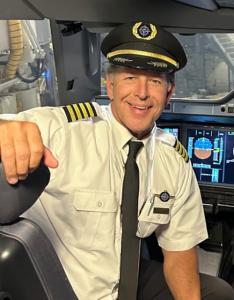 Captain Rob Islava sitting in an aircraft cockpit wearing a commercial airline captain’s uniform, smiling.
