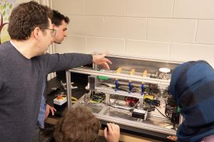 An image of a scientist demonstrating the Alpha-E device to students