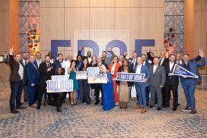 Group of people in front of brown wall with the word EDGE printed in big letters. Some group members holding signs and celebration items.