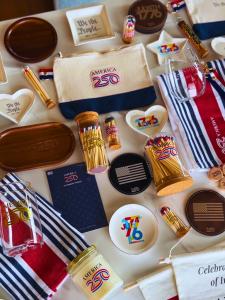 Flat lay of Thankful Greetings America 250 commemorative goods including match vessels, candle, glassware, trays, and accessories celebrating the United States 250th anniversary.