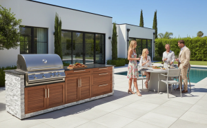 Premium outdoor kitchen with wood panel finish and stone accents next to a pool with people entertaining