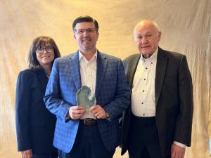 Three professionals at an award gala pose with their award.
