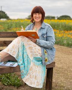 Smiling woman sitting on a bench holding a notebook in a field of flowers