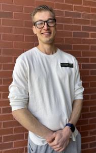 Max Radovanic of Mile High Compounds smiling in a casual setting against a brick wall, reflecting confidence and leadership in wellness innovation