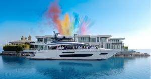 Superyacht brokers in Fort Lauderdale, Florida, standing on the deck of a superyacht, docked in front of a modern waterfront estate on the intra-coastal with colorful smoke flares in the background.