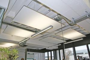 Modern office interior featuring a suspended acoustic ceiling system with large white rectangular sound-absorbing baffles. The panels are integrated with linear LED lighting and exposed industrial ductwork to reduce noise in an open workspace.