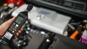 A technician in high-visibility gear performing a sound level test on a large industrial generator. Using a handheld decibel meter, they are conducting an acoustic assessment to ensure the machinery meets noise compliance standards.