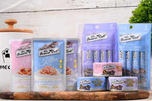 Fussie Cat Super Premium kitten wet food product lineup including pouches, squeeze tubes, and cans in pink, blue, and lavender packaging, displayed on a wooden tray against a white wood background.