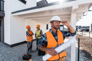 Project manager holding the blueprints looks ahead while colleagues with tools discuss in the background