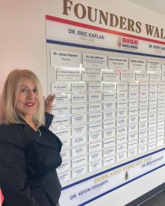 Grace Becerra, President of North American Medical Corporation, pointing to NAM’s name on the Founders Wall at the DISC Centers of America / LIFE University Outpatient Clinic and Educational Center.