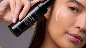 Close-up of a model applying Revision Skincare D·E·J Daily Boosting Serum to her cheek, highlighting the product’s lightweight texture and radiance-enhancing formula.