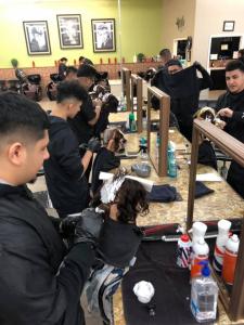 A row of cosmetology students in black smocks and gloves practicing hair highlighting and foil application on mannequin heads. The students are working at a professional salon station with mirrors and styling products at Lawrence & Company College of Cosm