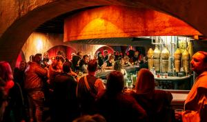 A wide photo of the warmly-lit Tangent Gallery bar, filled with costumed patrons and retrofitted with arched alcove booths, bartop, and barback props inspired by the Mos Eiesley cantina scene from Star Wars