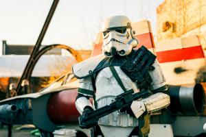 A character actor in full imperial stormtrooper cosplay poses near a prop inspired by the Star Wars A-wing starfighter in an outdoor market area at sunset